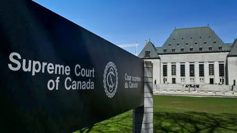 The Supreme Court of Canada sign with the name in both English and French in the foreground, with the court building behind it on a sunny day in Ottowa in May 2025. 