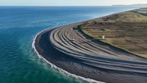 The coastline at the Point of Ayre, which has a rounded pebble beach with a lighthouse and fog horn.