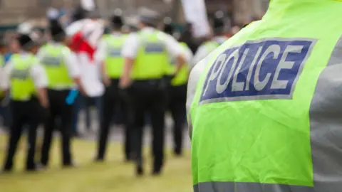 Getty Images A picture of the back of a police officer wearing a green jacket with "police" on the back of it, with five others further away from the camera. They are not in focus and are blurred.