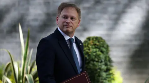 EPA Grant Shapps walking down the road in Downing Street carrying a dark red cabinet folder