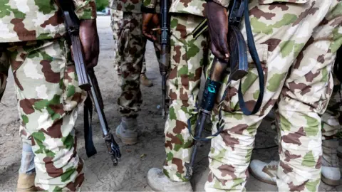 The legs of Nigerian soldiers in camouflage uniform and desert boots some holding weapons
