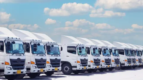 Getty Images A row of white HGVs against a backdrop consisting of a blue sky and clouds