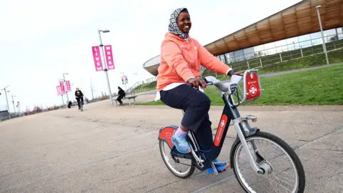 TfL Samra Said from Cycle Sisters riding the bike which has been named after her. She is wearing a black and white hijab and a coral pink jumper.