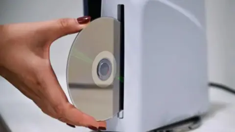 A woman's hand putting a disc into a PlayStation console.