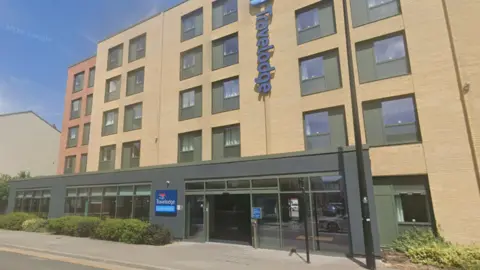 Google Google shot of a Travelodge hotel in Lincoln city centre. It is a modern, yellow-brick building with a glass-fronted entrance and the firm's logo displayed on the front wall and next to the entrance.
