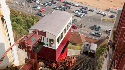 Getty Images A view from the top of the Leas Lift looking down to the beach over the top of one of the red and white cars.