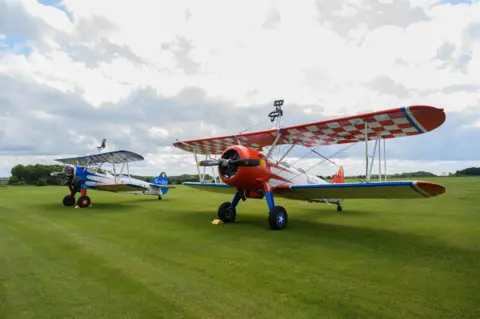 PA Two aeroplanes with colourful wings on green grass. 

