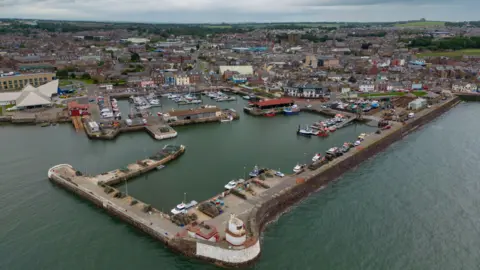 An aerial view of Arbroath showing its harbour and houses and other buildings that line the harbour and go back inland.