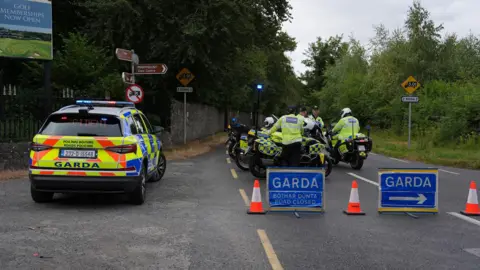 PA Media Police officers at the scene of the fatal crash in Dublin. Two of the officers are on motorbikes and a Garda car is also visible as are two blue Garda signs