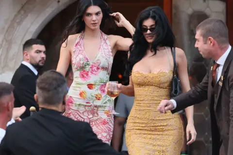 Getty Images Kylie Jenner and Kendall Jenner in Venice, Italy, for the wedding of Jeff Bezos and Lauren Sanchez. Kendall is wearing a floral print dress and Kylie is wearing a yellow dress. 