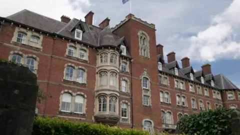 A red brick building with gothic stone windows, under a blue, cloudy sky