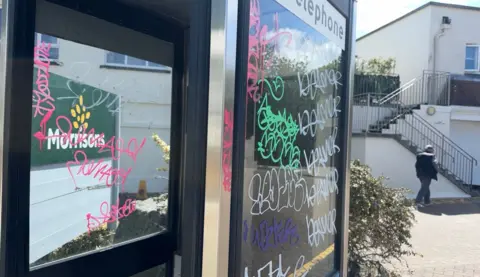 A unused phone box covered in white, green and pink graffiti