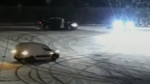 Peterborough City Council A screenshot of CCTV footage showing a white van doing doughnuts in a snow-covered car park.