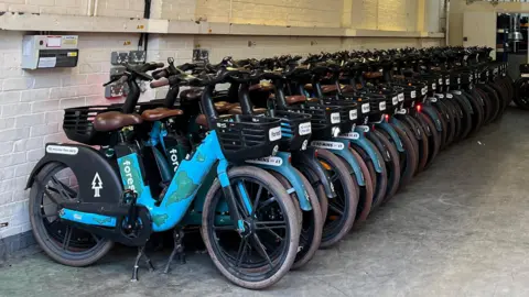 Line of blue ebikes fill a warehouse