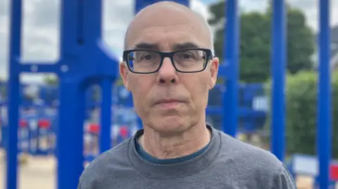 Dean Piacenti looking at the camera is wearing black framed glasses and a grey t-shirt.