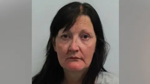 A police mug shot of Drina Gray, a woman with long dark hair