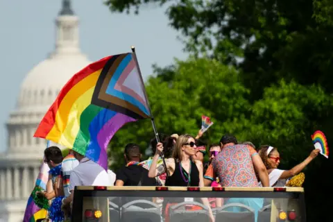 Parade participants wave rainbow flags from the top of a double decker tour bus as Capital Pride Parade makes its way down Pennsylvania Avenue in Washington DC. The dome of the US Capitol is in the background.