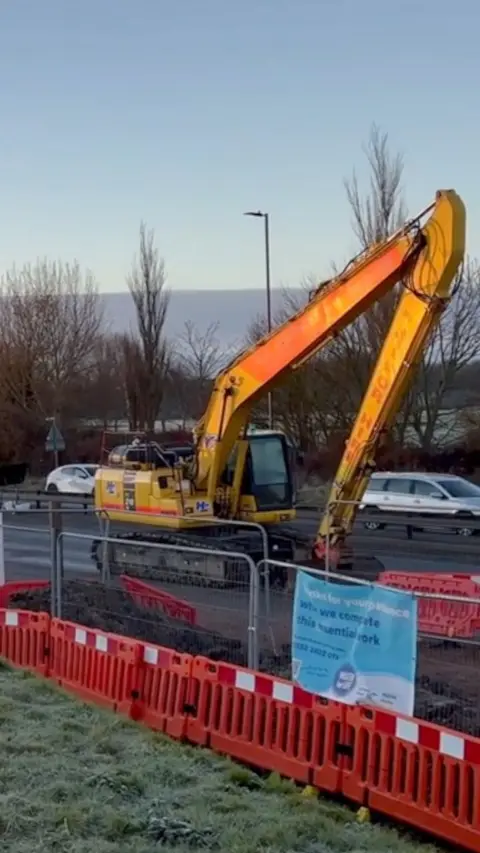 A large yellow crane surrounded by neon orange protective fencing and cars in the background in Eastern Road, Portsmouth.