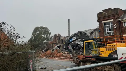 Chris Goreham/BBC Demolition plant alongside piles of red bricks