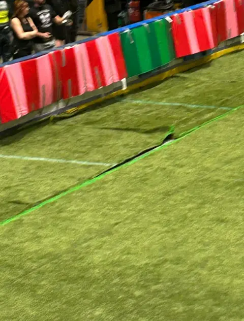 Artificial turf bunched up at the side of a playing surface