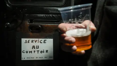 AFP via Getty Images A man holds a glass at a bar truck in the village of Villequiers, central France. Photo: March 2019