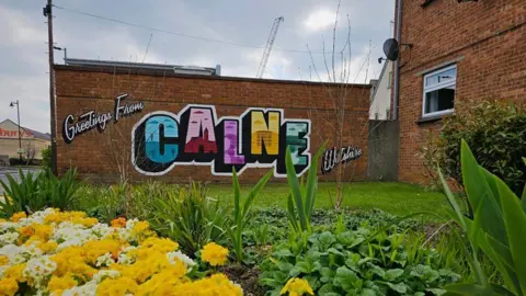 Calne Clean up Crew A colourful mural that says 'Greetings from Calne, Wiltshire' on the side of a building