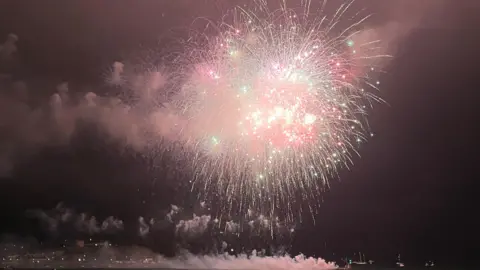 A picture of a large fire work exploding in the air. There is smoke surrounding the light.