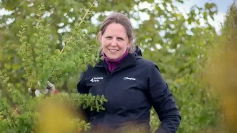 National Parks England A woman stood in some bushes.