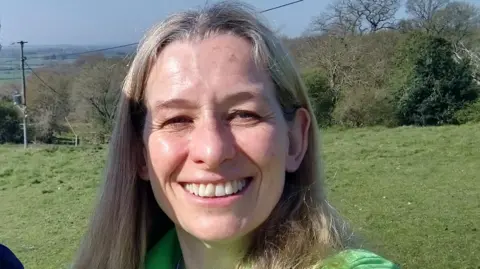Hill End Lucy Crittenden has long hair and is wearing a green t-shirt. She is standing in a large green open field.