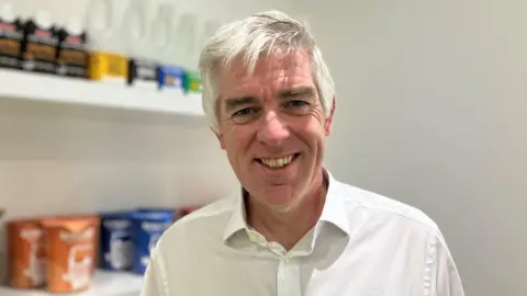 Man with white hair smiling at the camera, he is wearing a white shirt