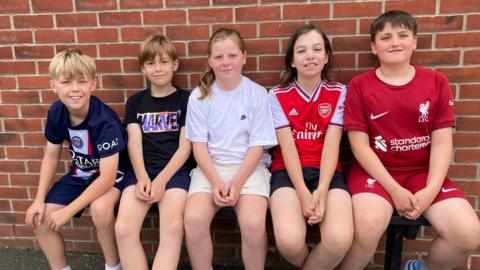 Five children sitting on a bench outside the school building