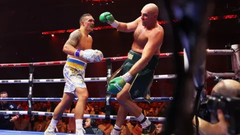 Tyson Fury is punched by Oleksandr Usyk and staggers backwads