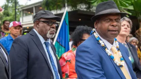 Pabai Pabai, right, and Paul Kabai, both elders from the Torres Strait Islands, wearing suits and hats. Pabai is wearing a traditional necklace, made of shells. 