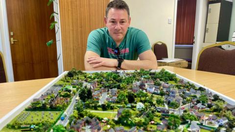 Man sits beside this scale model of Gnosall, Staffordshire.