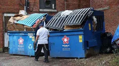 Getty Images a man stands in a white square with his back to the camera in front of two huge inflated waste, which is located behind a red brick building. Blue speakers have been placed with "Republic services" Red and white star logo.