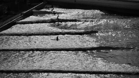 Ian McAteer Surfers practicing on the waves at a surf resort - the figures are silhouettes with the image in black and white. 