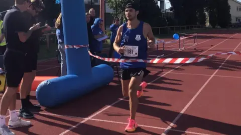 Mr Rice running over the finish line of a race. There are crowds cheering him.