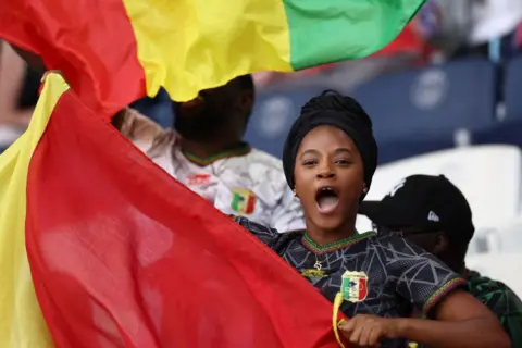 FRANCK FIFE/AFP A woman watching in the stands waves the Malian flag at a stadium in Paris, France - Thursday 25 July 2024