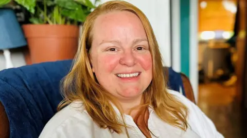 Woman, Marlene Lowe, with blonde hair, and white blouse, smiling at camera.