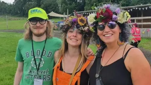 Shows a festival worker and two women wearing flowers in their hair