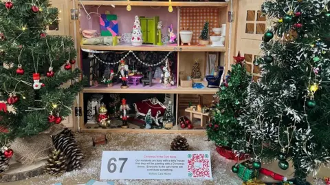 An open doll's house with a Christmas theme with two smaller Christmas trees in front