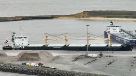 MV Ruby pictured inside Great Yarmouth's outer harbour, taken from a drone. The picture shows the breakwaters of the harbour, and a blue vessel adjacent to MV Ruby