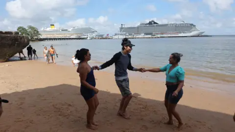 Reuters Cruiseschepen, gebruikt als accommodatie voor COP30 in de rivier. Voor hen staan ​​drie mensen op het strand.