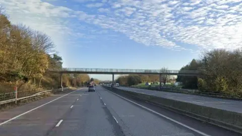 A Google Maps view of the affected part of the M4. The eastbound side of the road has three lanes running across it and a bridge spanning the full width of the motorway. There is not much traffic, and the picture has been taken on a sunny day with light wispy clouds. 