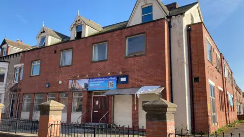 A rundown-looking two-strorey red-brick building.