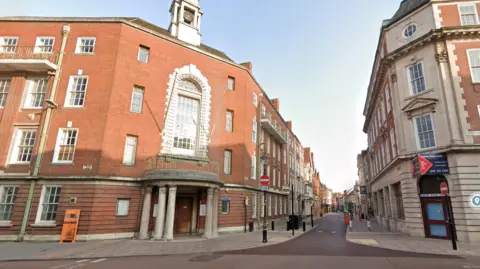 The exterior of Grey Friars in Leicester. A red brick building with white windows and a clock on the roof.