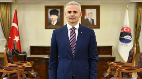 Ardahan Governorship Çiçekli standing in his room wearing a floral navy suit