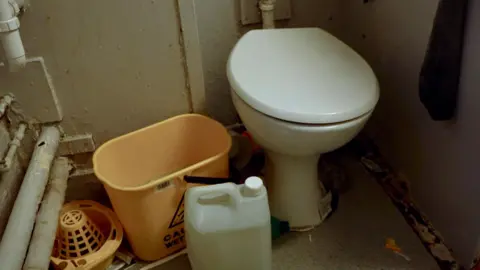 A filthy and leaky toilet from one of the cells in Pentonville. Cleaning products and a mop bucket are seen next to it.