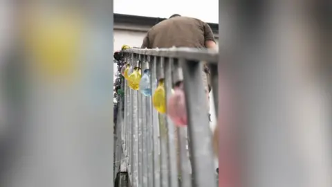 A man in a brown t-shirt stands at the top of a metal staircase