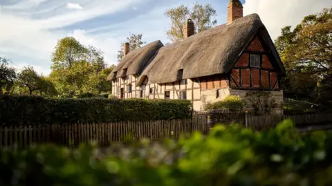 Sam Allard A large thatched house sits in a large garden.